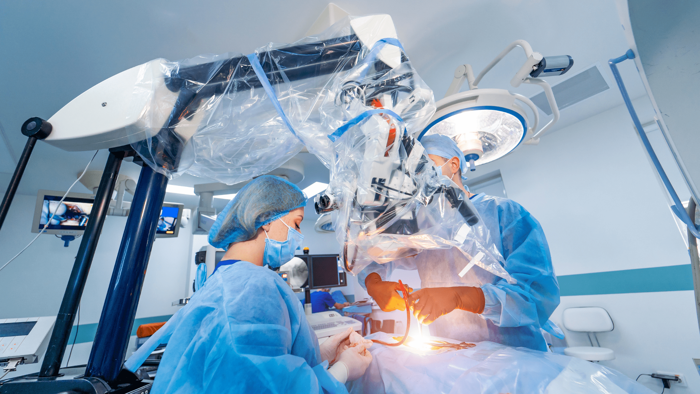 Two surgeons, one female, one male, work under a surgical robot.